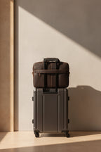 The briefcase resting on a suitcase in an airport, its rear luggage strap shown in an inset detail