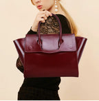 The wine red leather tote carried by hand, showing its scale against the body
