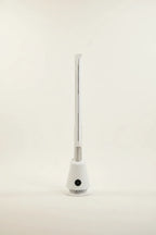 White bladeless tower fan standing on a grey floor in a home office, beside a desk and window