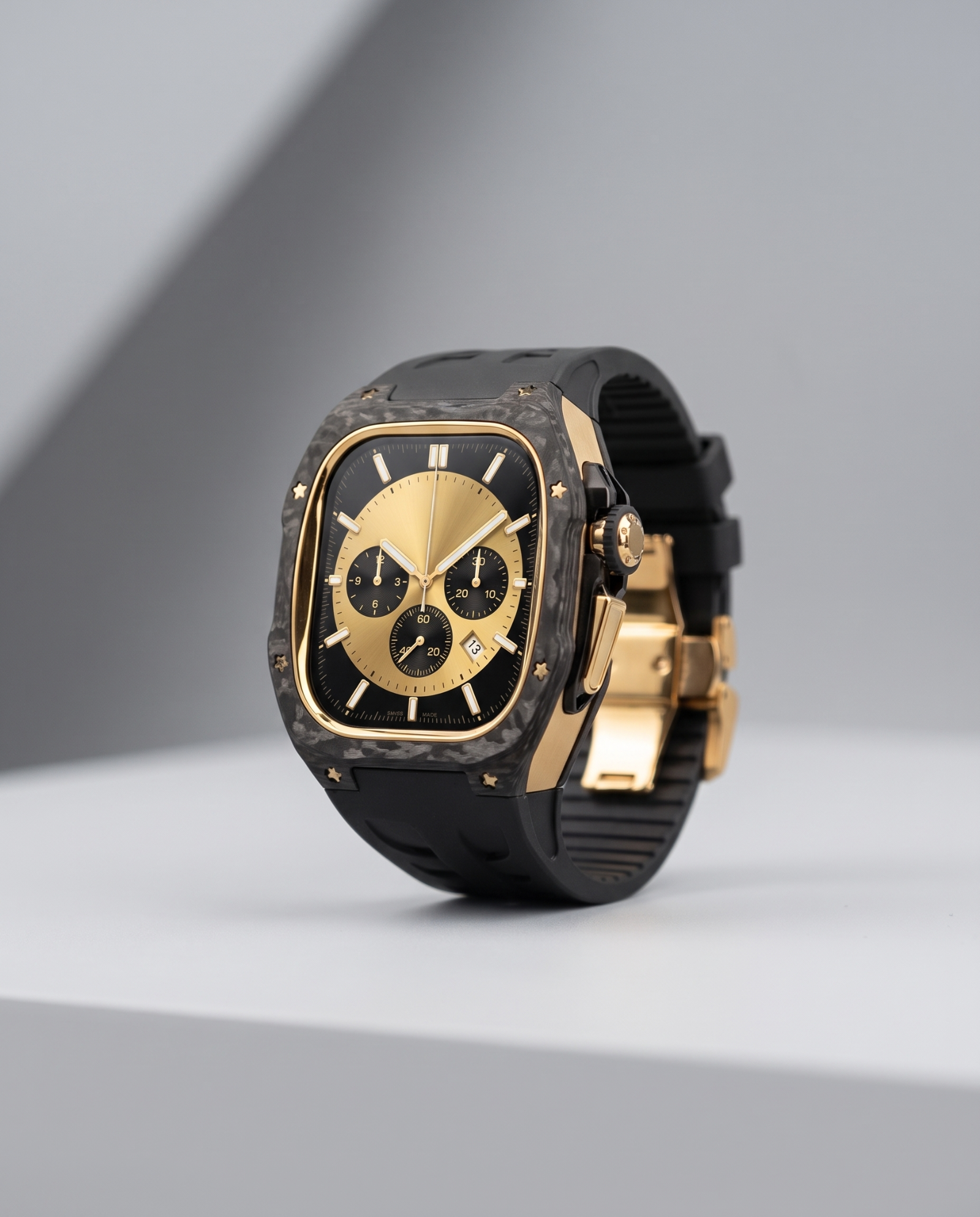 A luxury Apple watch Kit with a black and gold-tone case, and a black carbon-fiber bezel, displayed on a light gray platform against a gray background.