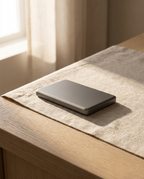 The dark grey power bank resting on textured cloth on a light wood table in soft window light