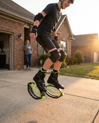 Teenager bouncing on a driveway in black and green bounce jump shoes while a parent watches