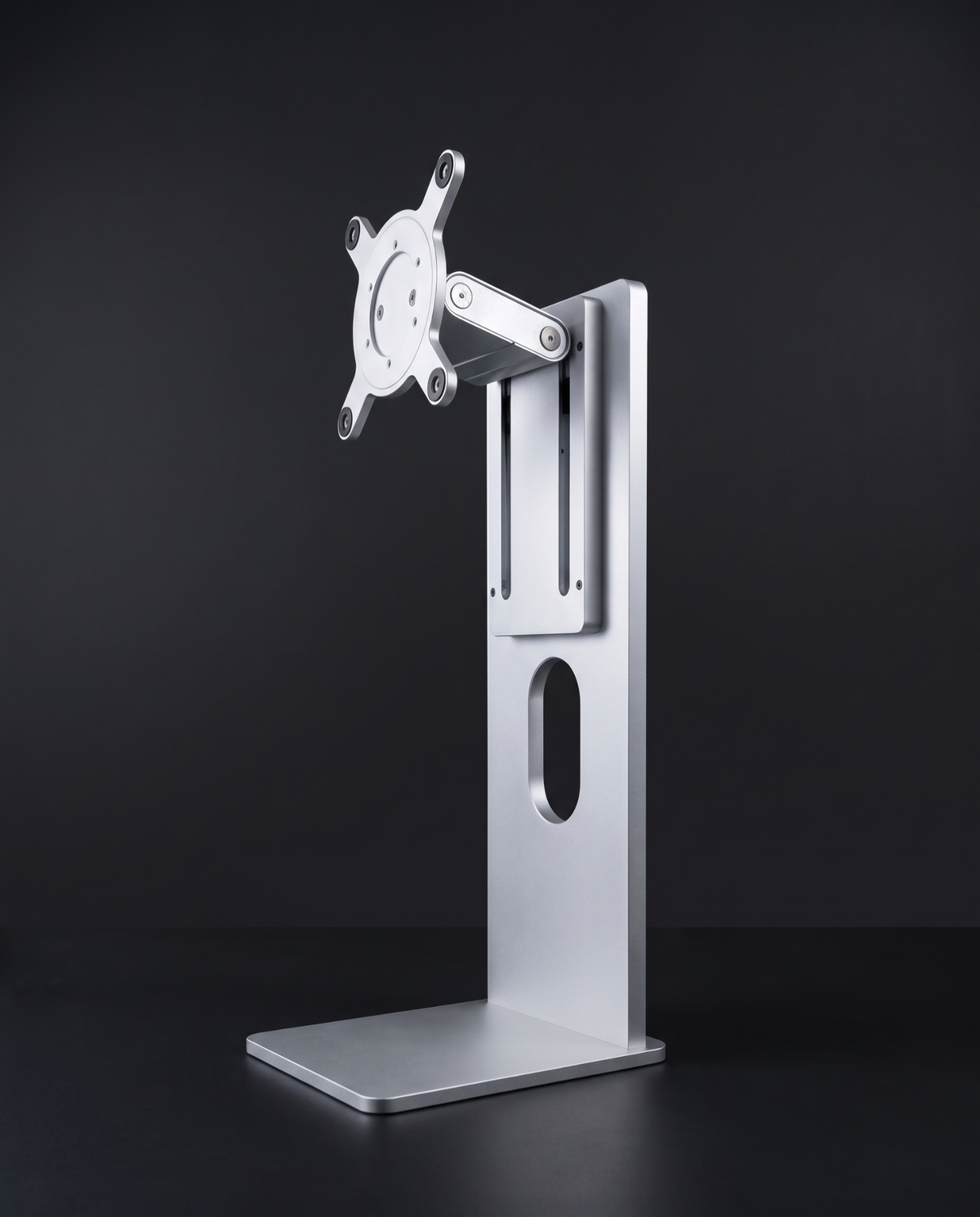 Aluminium monitor stand with VESA 100 plate and hinge arm, three-quarter view on graphite