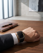 Man at a desk in a modern office wearing the case kit on a black strap, beside a leather folio and fountain pen
