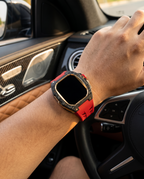 Man driving a luxury car wearing the case kit on a red strap, hand resting on the steering wheel