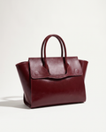 A burgundy leather handbag with double top handles and a front flap, photographed on a clean white studio background.
