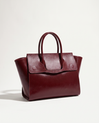 Wine red full grain leather tote with double top handles and a front flap, shown against soft white