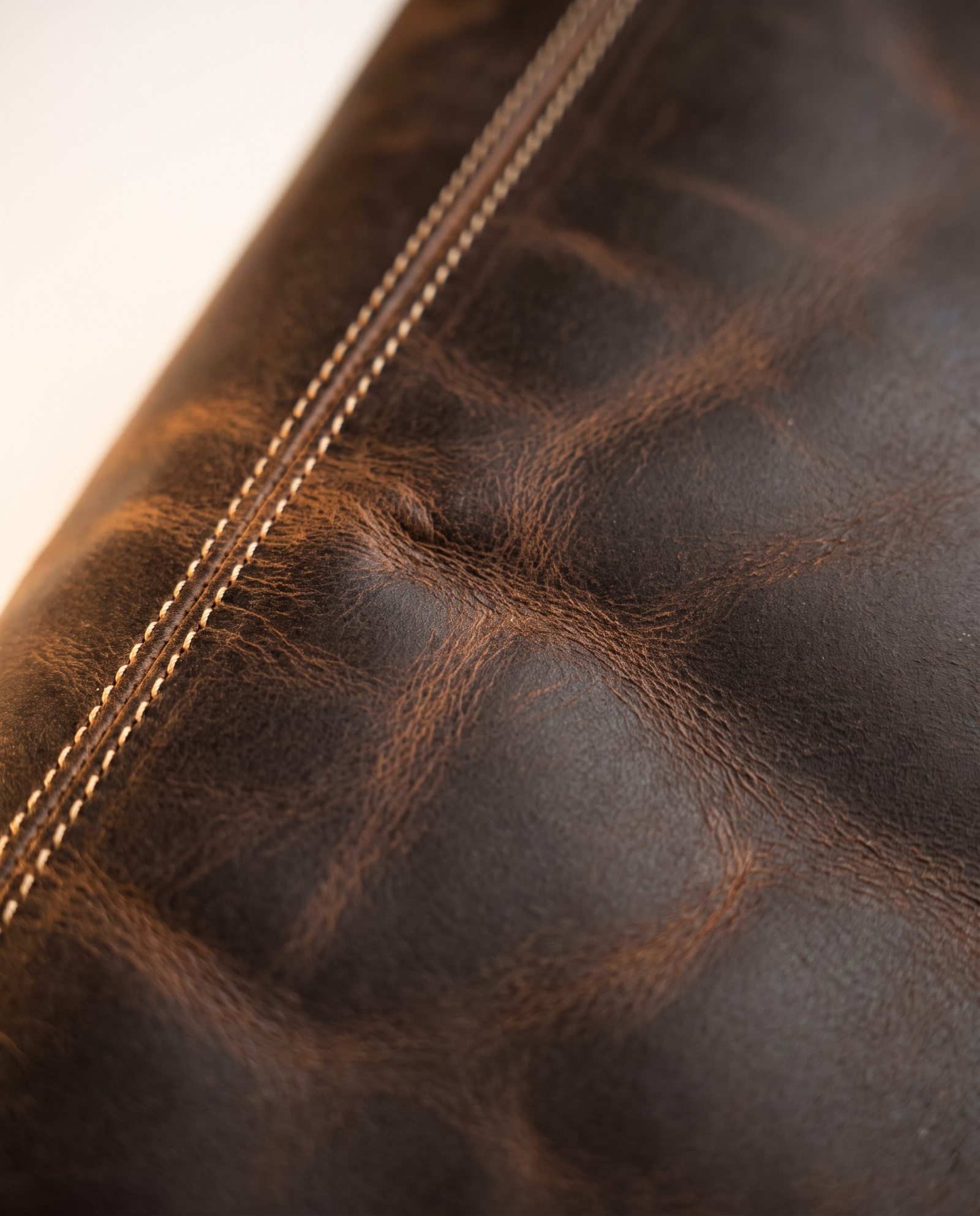 Macro close-up of dark brown crazy horse leather grain, patina and edge stitching