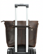 The tote's front zip pocket, shown with a rolling suitcase handle passed through the luggage strap