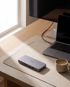The docking station on a desk mat beside an open laptop and a coffee cup in natural window light