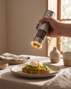 A hand grinding pepper over avocado toast with a poached egg, the mill lit from within