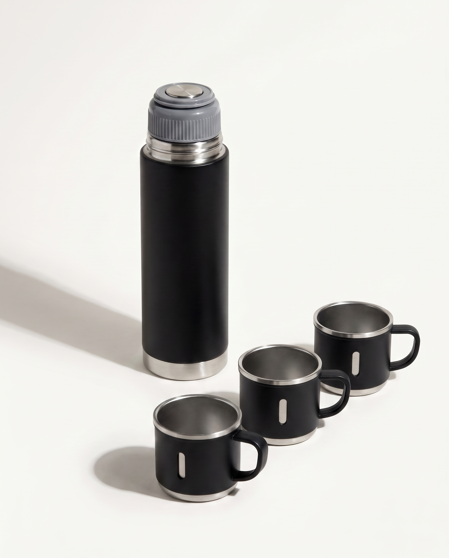 Matte black insulated vacuum flask gift set — 500 ml flask with grey spill-proof inner lid and three stainless-rimmed cups on a soft white background