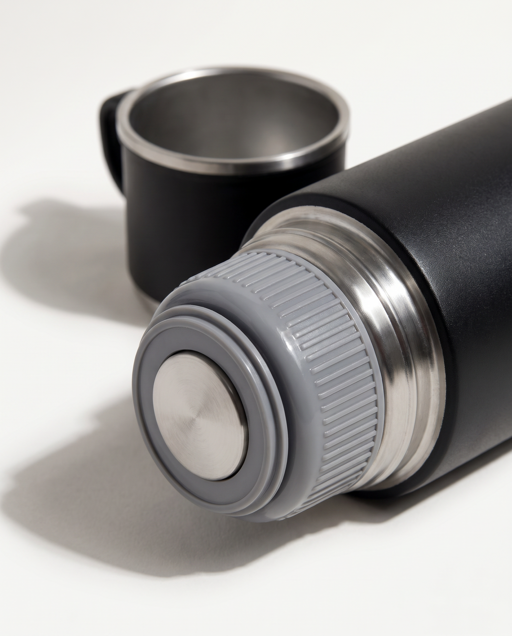 Macro detail of the spill-proof lid — grey food-grade inner lid with stainless steel button, ribbed threads and silicone sealing ring