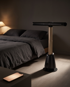 The tower fan beside a low bed at night, a phone glowing on the nightstand for app control