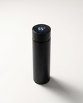LED thermos cup in black, lid display lit and reading 55°C, on a soft white studio background