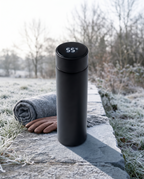 The LED thermos cup on a frosted stone wall on a cold morning, display lit beside a wool scarf