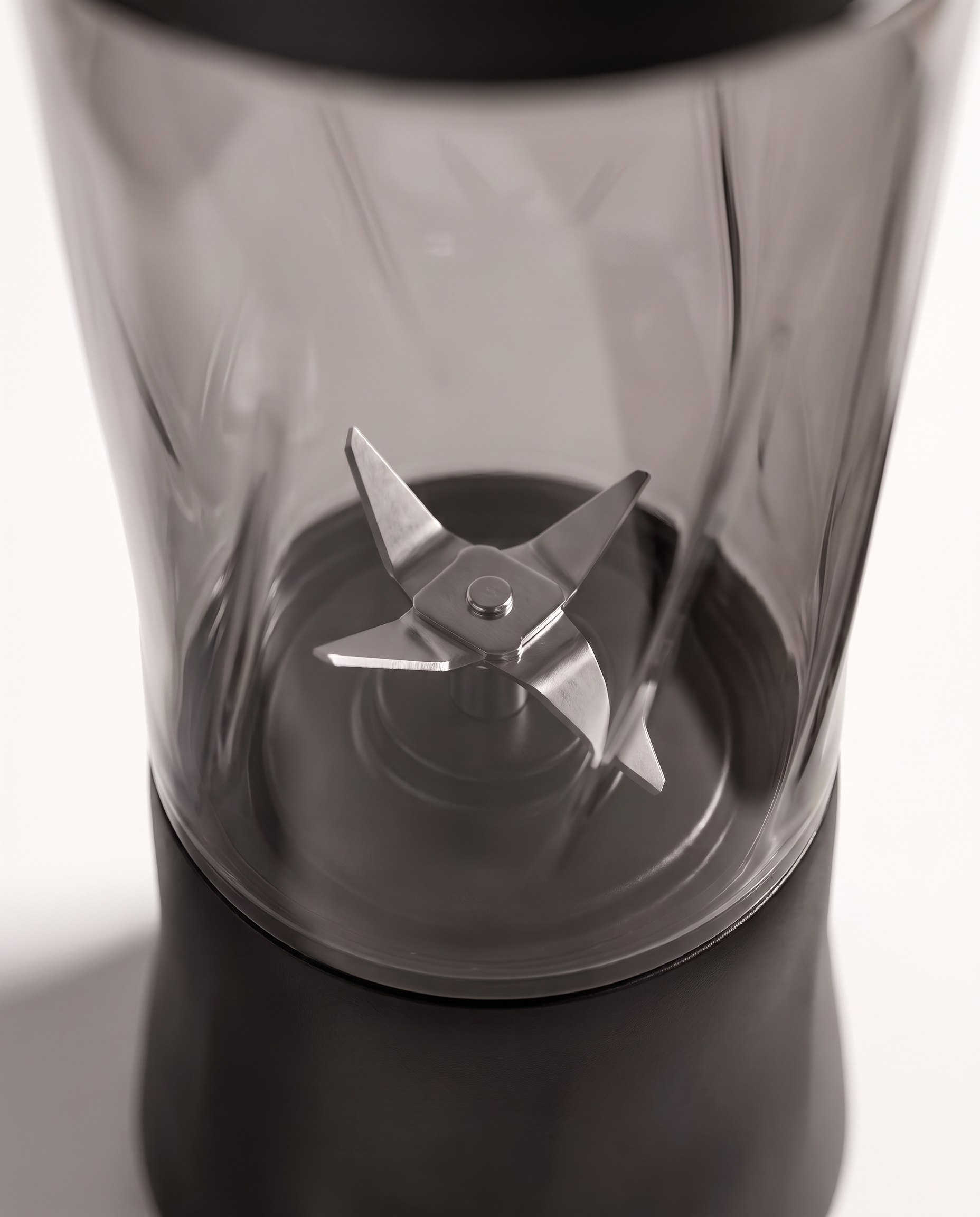 Macro detail of the six-point stainless steel blade assembly seen through the tinted bottle wall