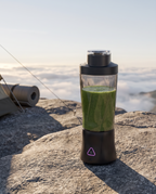 The portable blender on a granite slab above a cloud-filled valley at dawn, filled with a green smoothie