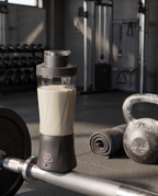 The portable blender in a gym beside a barbell and kettlebell, filled with a protein shake