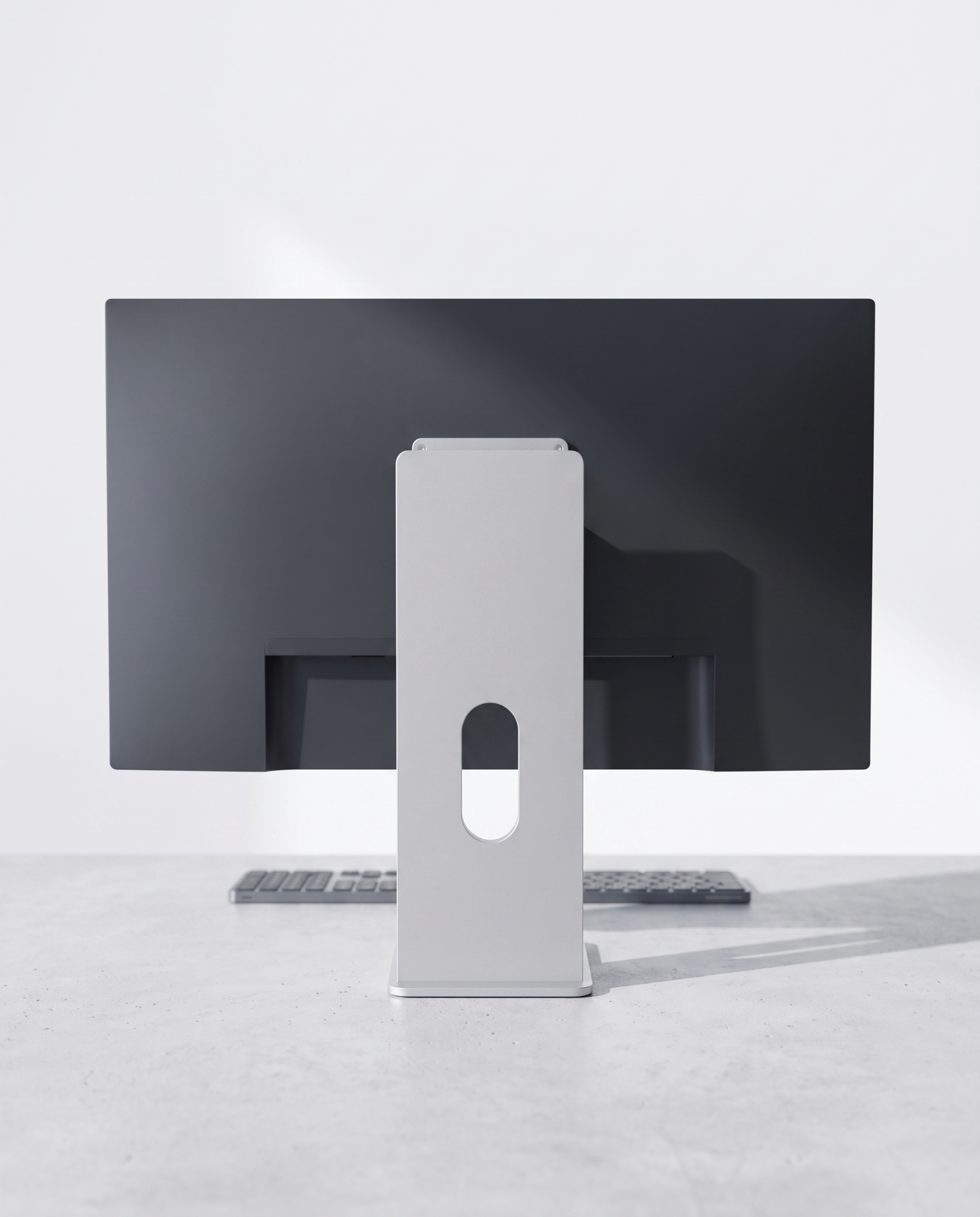 The aluminium monitor stand on a pale concrete desk in a bright studio workspace at midday.