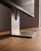 Low angle view along the desk, the weighted base close in the foreground and the aluminium column rising behind it.