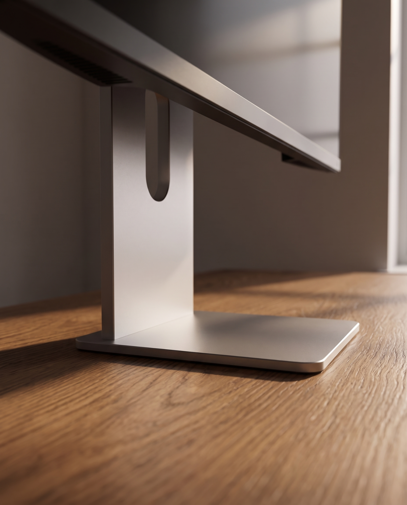 Low angle view along the desk, the weighted base close in the foreground and the aluminium column rising behind it.