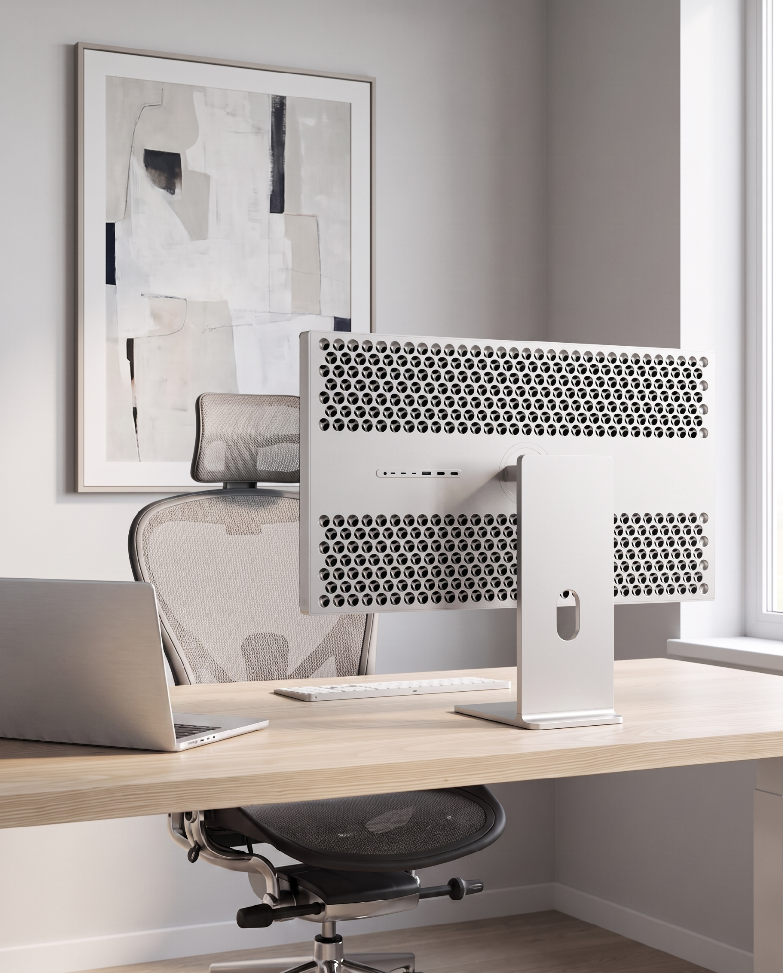 A modern white desktop computer monitor with a distinctive honeycomb-patterned backplate sits on a light wood desk in a bright home office setup, alongside a laptop, keyboard, and mesh office chair.
