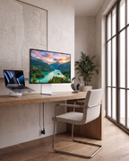 A modern home office setup featuring a sleek desktop monitor displaying a mountain lake landscape, paired with a laptop, headphones, and a white upholstered chair with a chrome frame, set against a warm beige textured wall and large window.