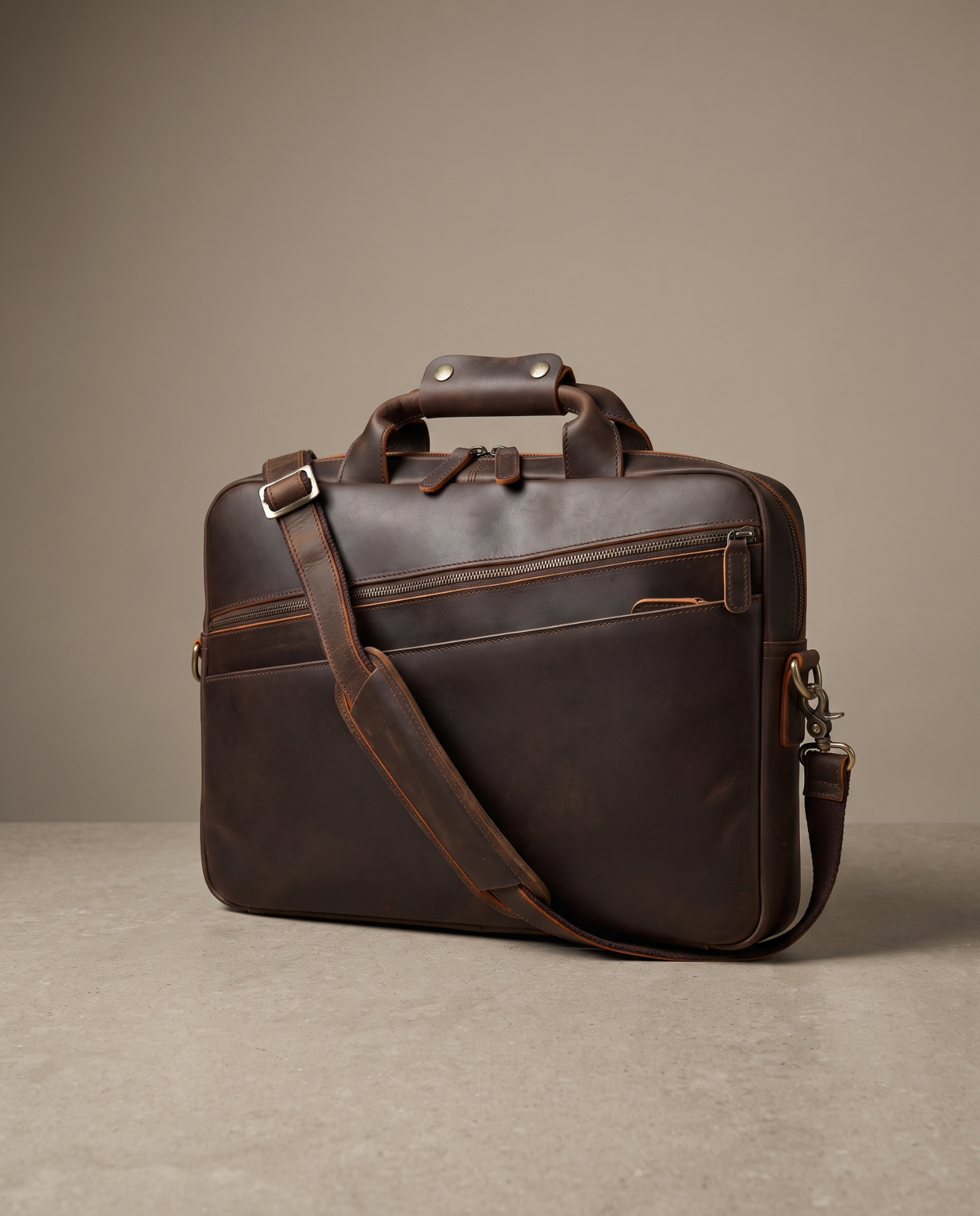 A dark brown leather briefcase with a top handle, a detachable shoulder strap, and a front zippered pocket, photographed on a neutral beige studio background.
